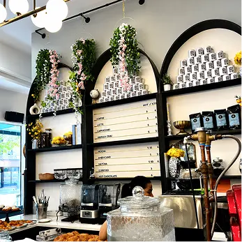 A cozy café with arched shelves, hanging plants, a menu board, and a counter with coffee-making equipment.