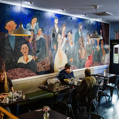 People dining in a restaurant with a colorful mural of people on the wall.