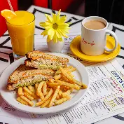 A plate of sandwich and fries, a cup of coffee, a glass of orange juice, and a yellow flower on a table.